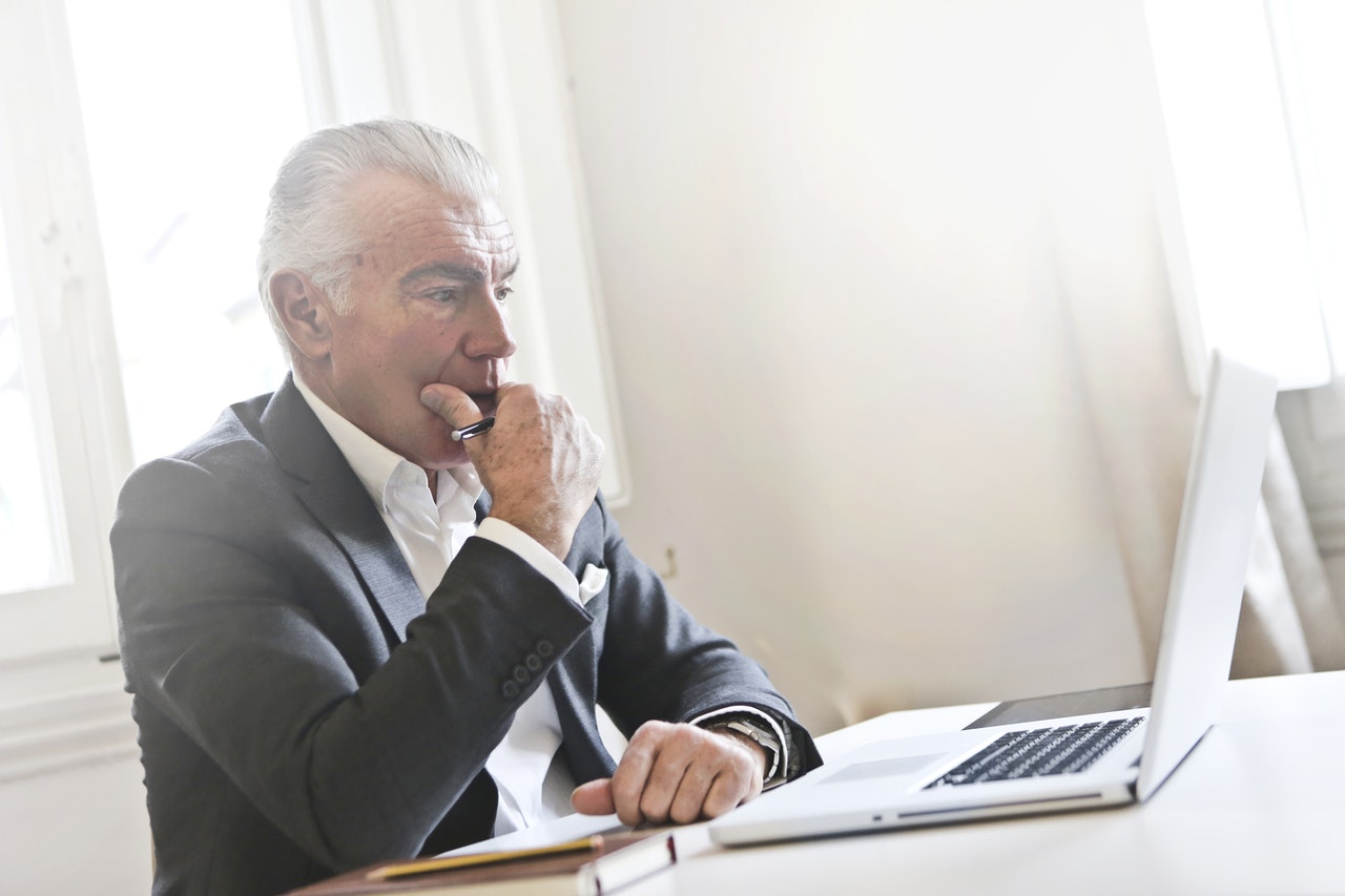 Older man in suit coat staring at laptop planning his retirement.