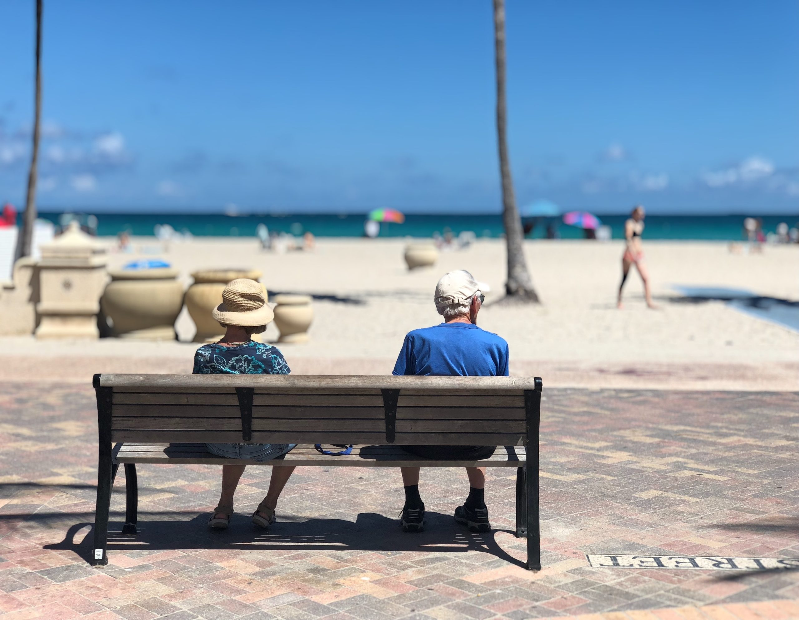 Two older people sitting on a bench looking out at the beach.